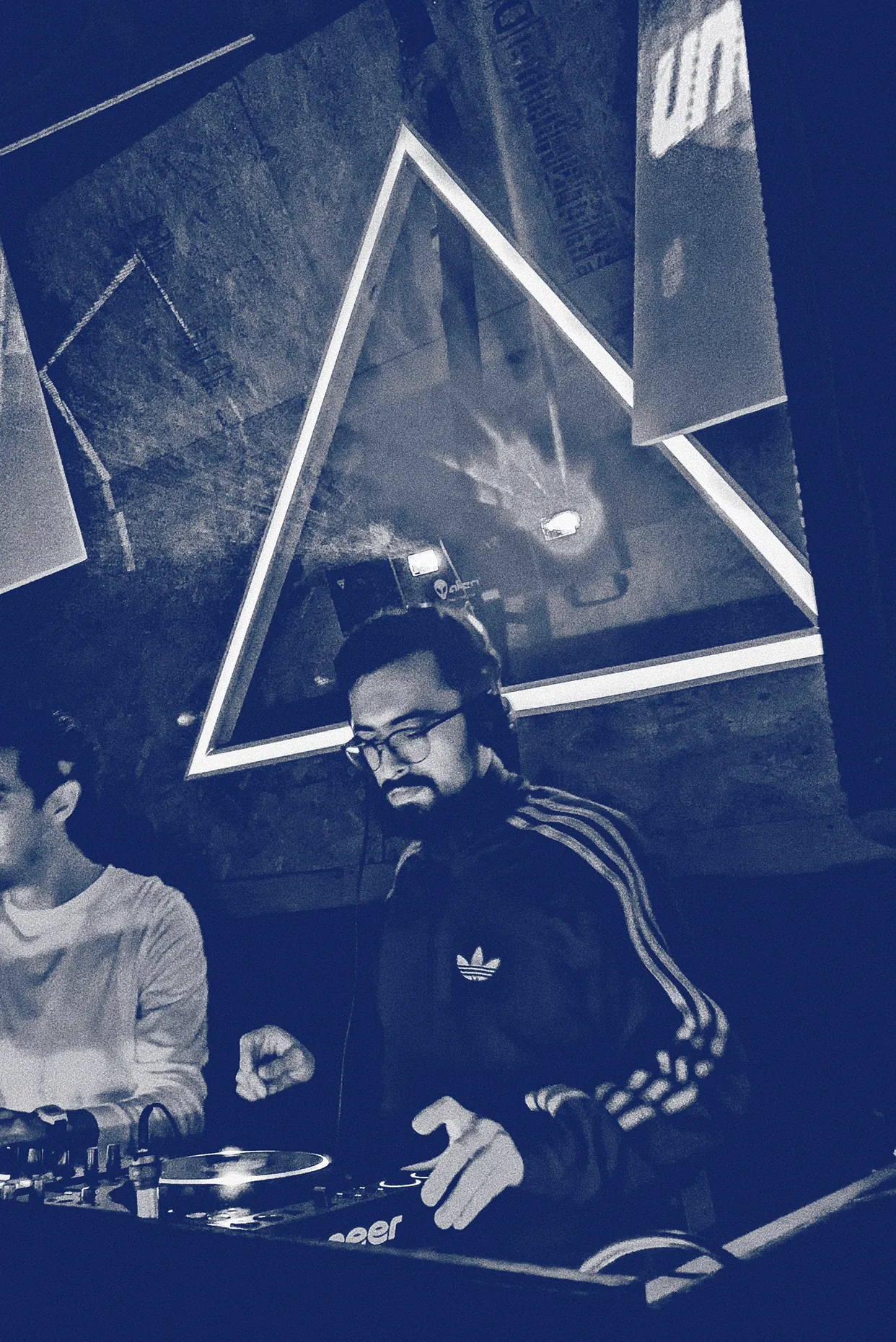 Marc DJing in headphones, under a lit triangle